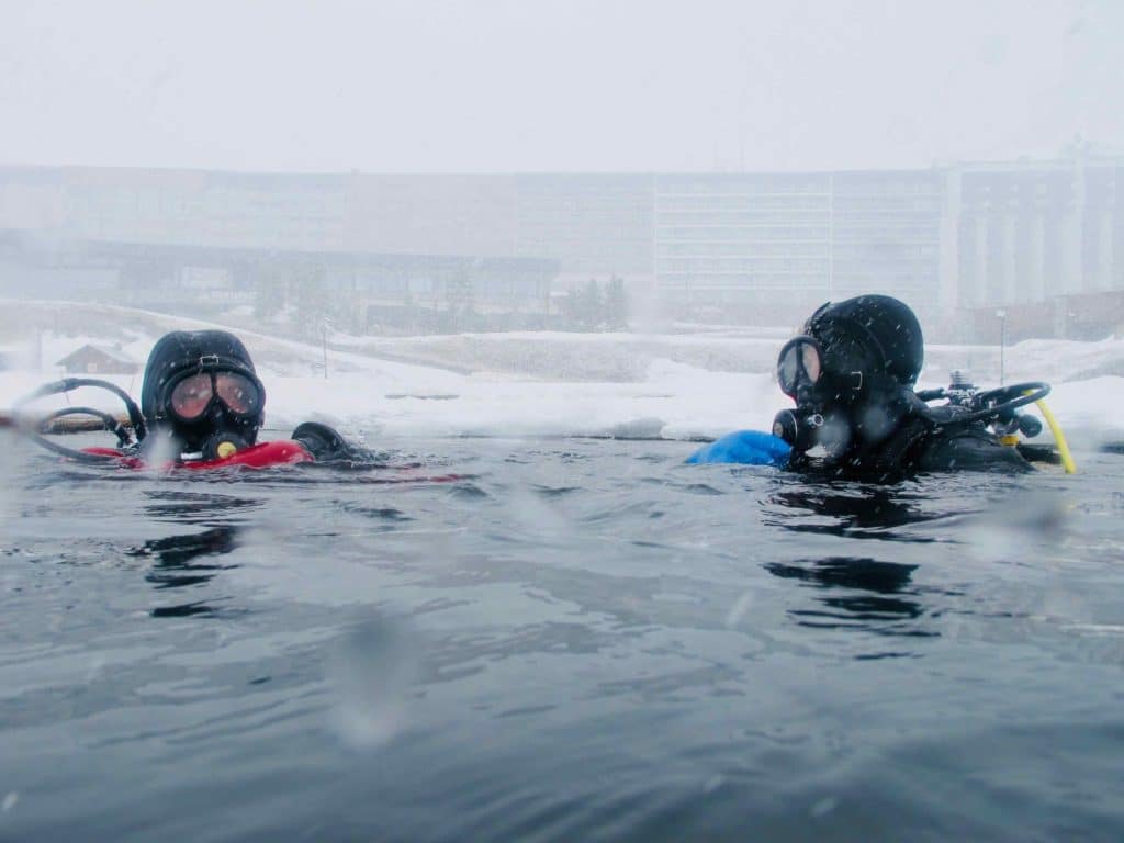 Deux plongeurs sous glace à Tignes entrent dans l'eau. Une des 10 idées plongée pour l'hiver.
