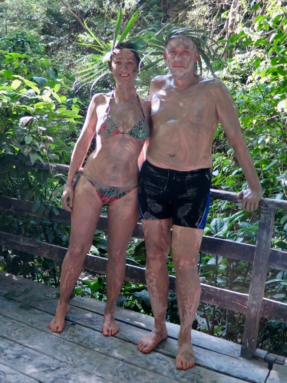 Un couple se tient dans la jungle couvert de boue avant de s'immerger dans des thermes naturelles