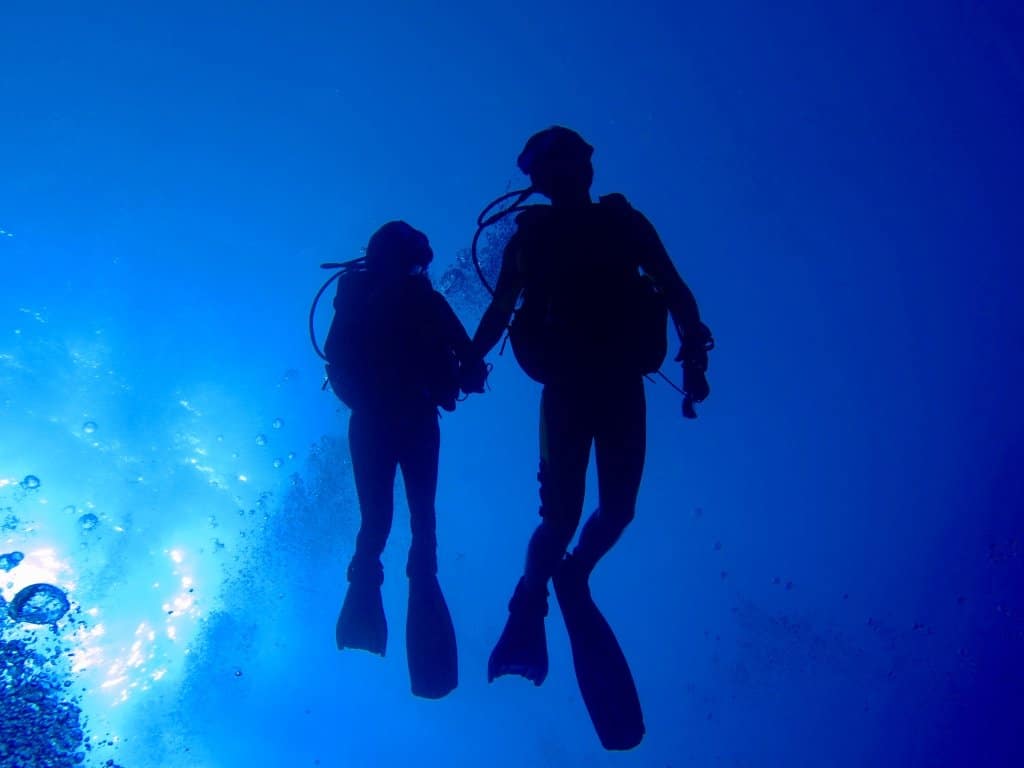 Des jeunes plongeurs occupés à plonger en couple se donnent la main sous l'eau.