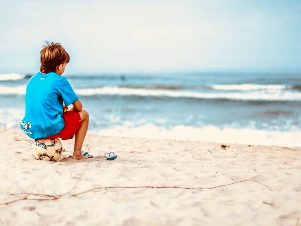 Un enfant assis sur sa balle de football regarde l'océan