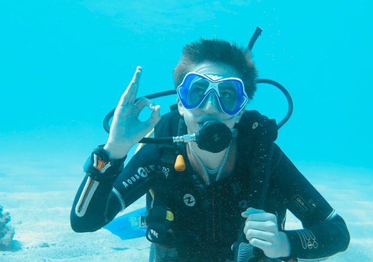 Un jeune plongeur fait le signe ok sous l'eau