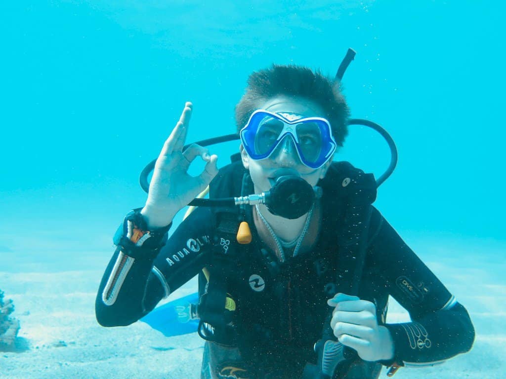 Un jeune plongeur fait le signe ok sous l'eau