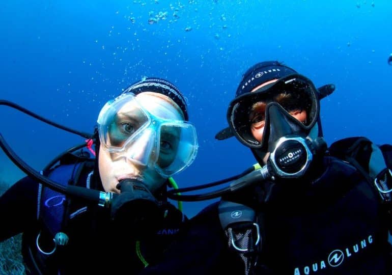 Un plongeur et une plongeuse se prennent en photo sous l'eau lors d'une plongée pour exprimer l'amitié en plongée.