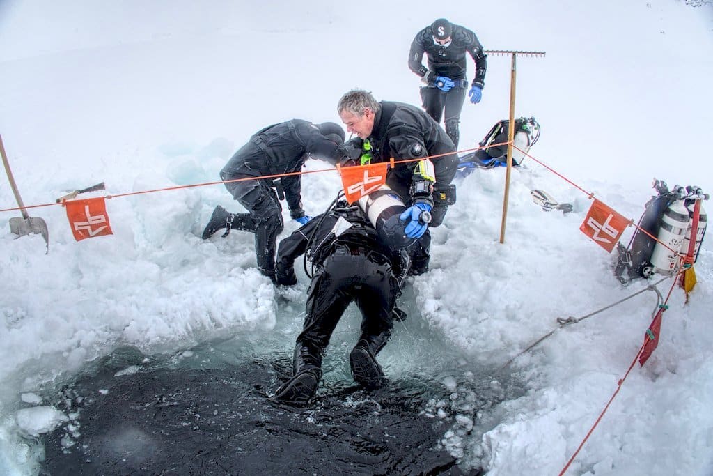 Des plongeurs aident un autre à sortir de l'eau gelée.