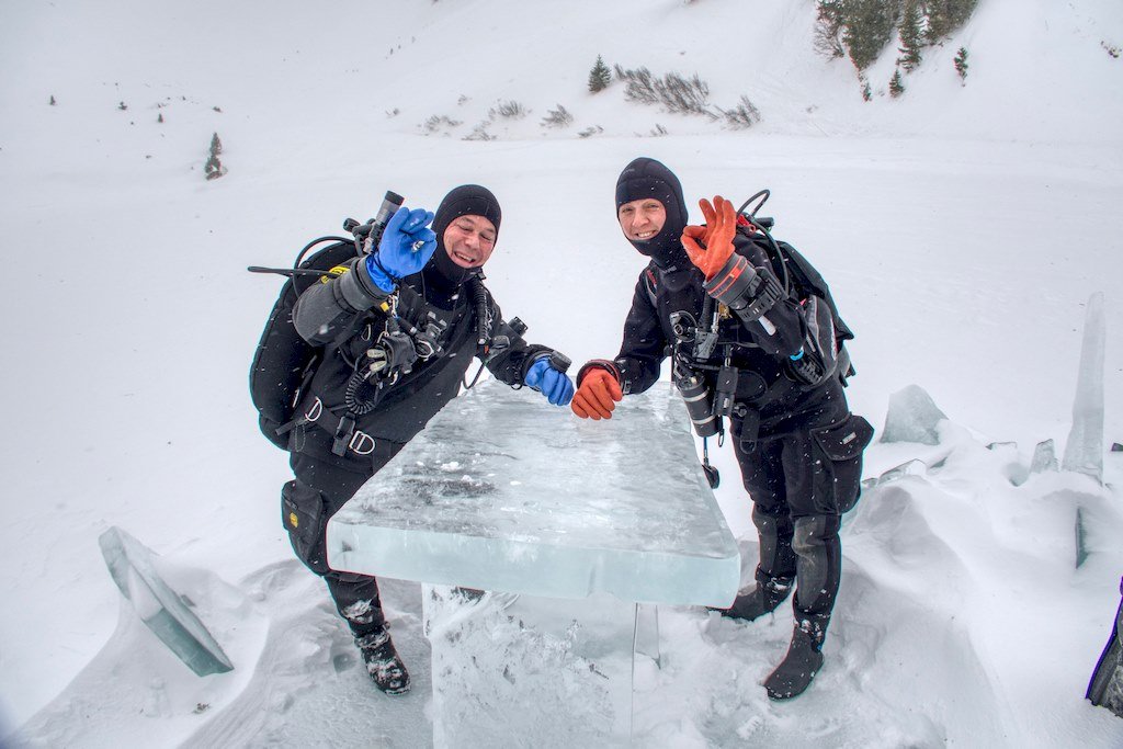 Deux plongeurs font le signe OK autour d'une table sculptée dans la glace.