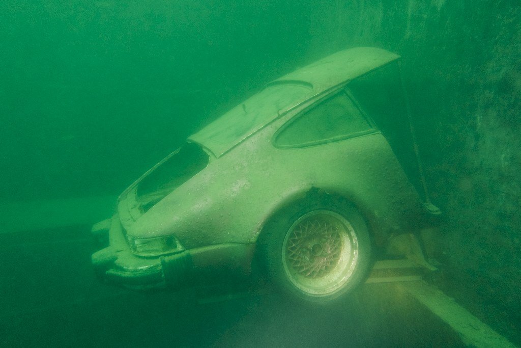 Une demi Porsche immergée dans l'eau de la carrière