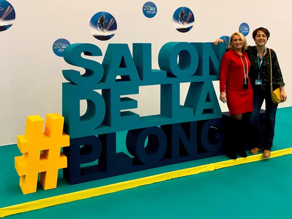 Hélène Adam et Hélène de Tayrac pose devant l'insigne du Salon de la Plongée 2020