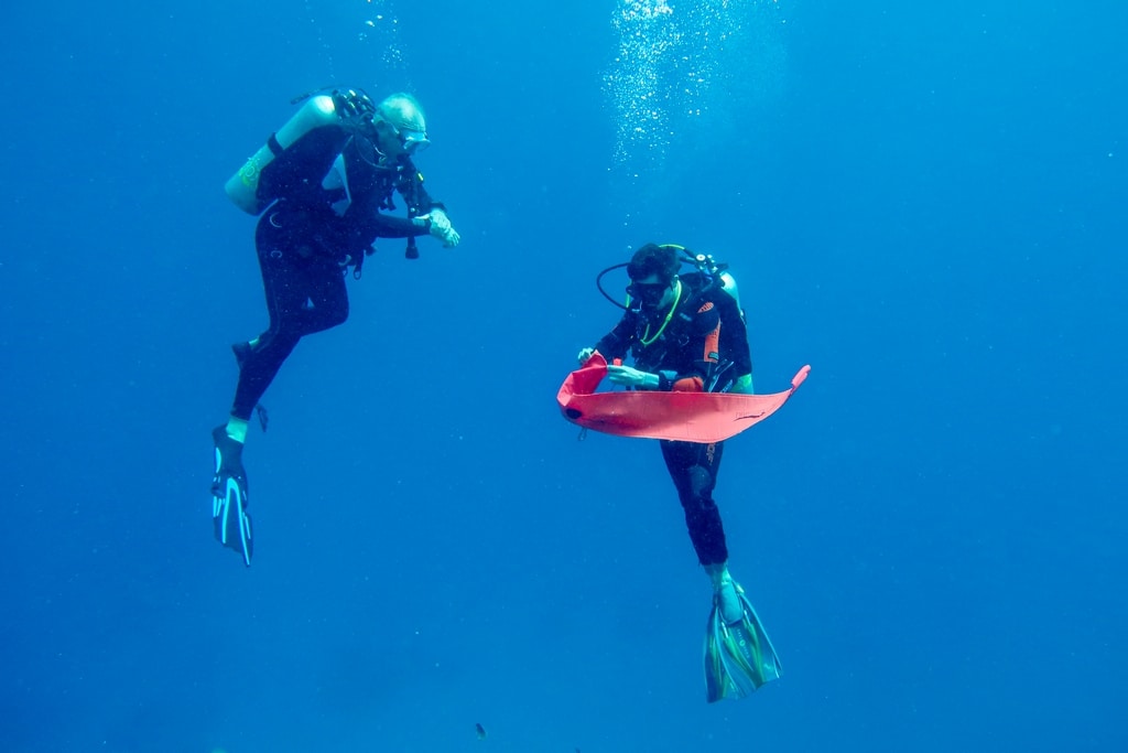 Deux plongeurs occupés à déplier un parachute de plongée en mer.